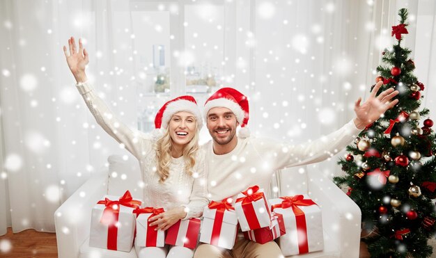 natal, feriados e conceito de pessoas - casal feliz em chapéus de papai noel com caixas de presente sentado no sofá em casa