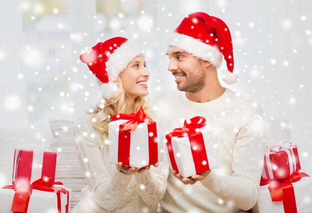 natal, feriados e conceito de pessoas - casal feliz em chapéus de papai noel trocando presentes em casa