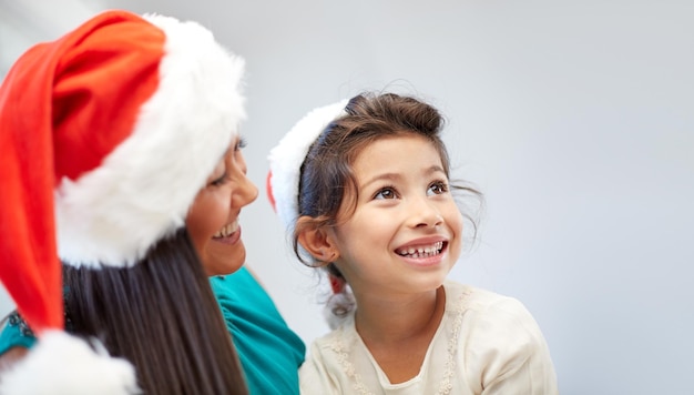 natal, feriados, família, infância e conceito de pessoas - feliz mãe e menina em chapéus de papai noel em casa