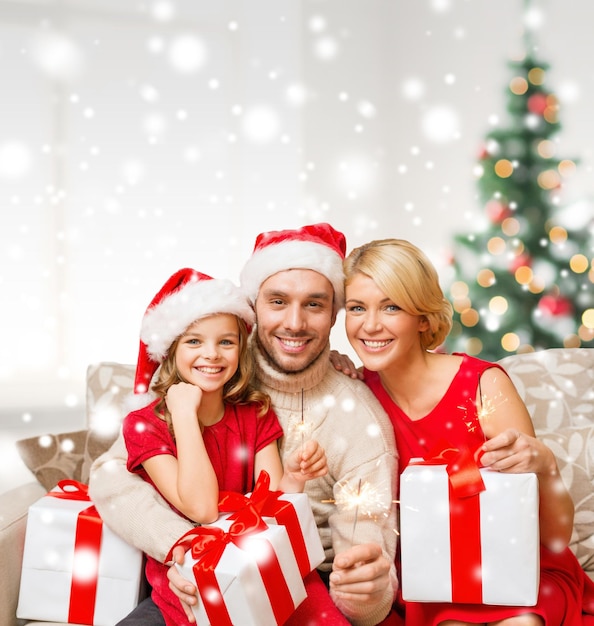 natal, feriados, felicidade e conceito de pessoas - família sorridente em chapéus de ajudante de papai noel com muitas caixas de presente e estrelinhas em casa