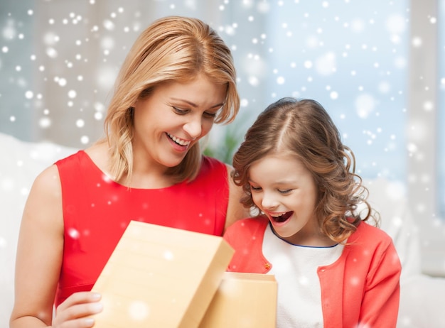 Foto natal, feriados, pessoas e conceito de família - sorrindo mãe e filha abrindo caixa de presente e se surpreendendo em casa