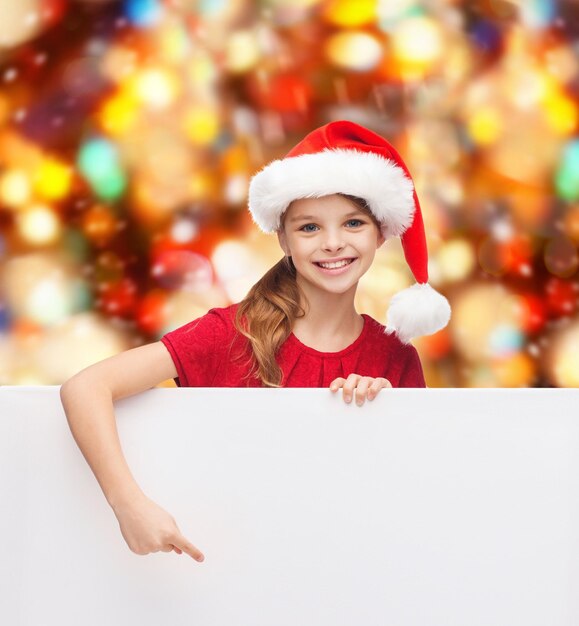 natal, feriados, pessoas, propaganda e conceito de venda - menina feliz no chapéu de ajudante de papai noel com quadro branco em branco sobre fundo de luzes vermelhas