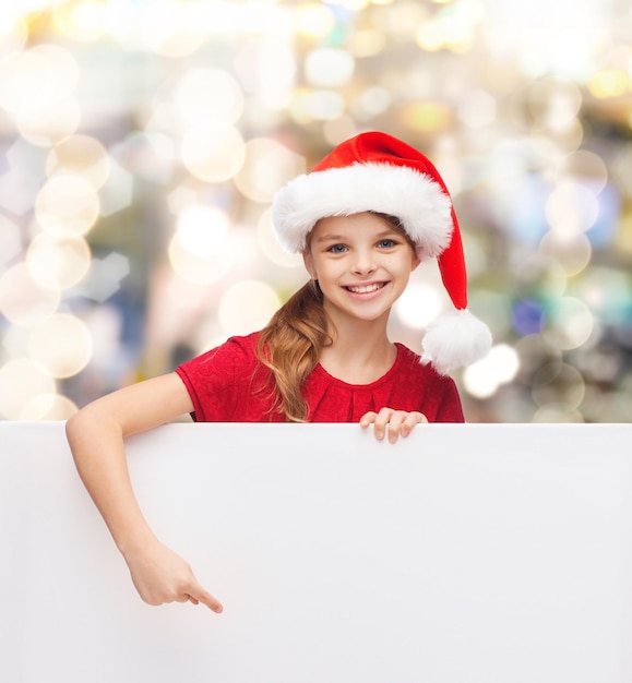 natal, feriados, pessoas, propaganda e conceito de venda - menina feliz no chapéu de ajudante de papai noel com quadro branco em branco sobre fundo de luzes