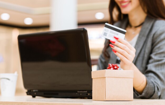 Natal, feriados, tecnologia e conceito de compras - mulher sorridente com cartão de crédito, caixa de presente e computador portátil sobre fundo de luzes. Foto horizontal