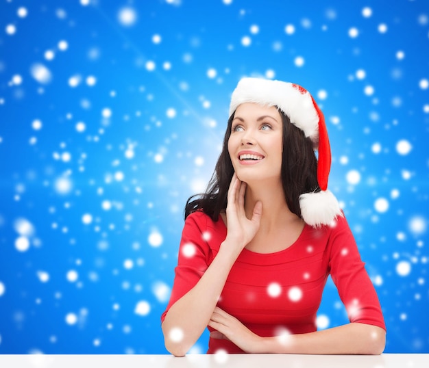 natal, inverno, feriados, felicidade e conceito de pessoas - mulher sorridente com chapéu de ajudante de papai noel sobre fundo azul nevado