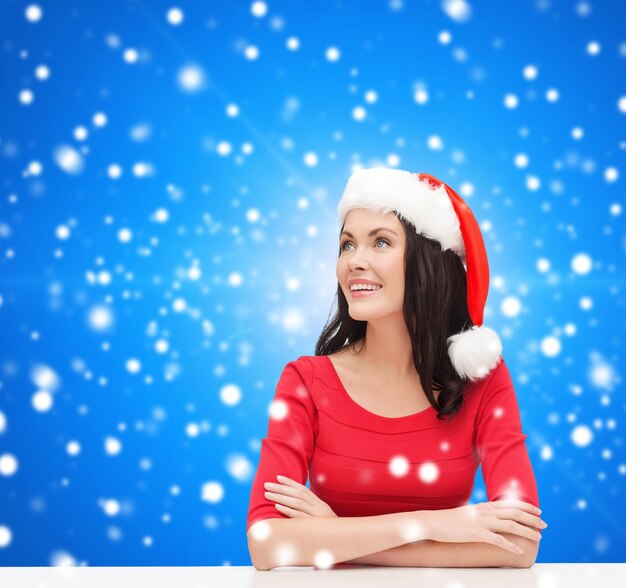 natal, inverno, feriados, felicidade e conceito de pessoas - mulher sorridente com chapéu de ajudante de papai noel sobre fundo azul nevado