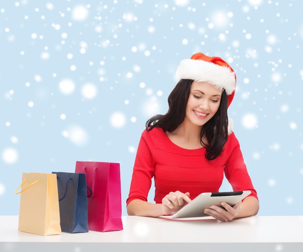 Natal, natal, conceito de compras online - mulher com chapéu de ajudante de papai noel com caixa de presente e computador tablet pc