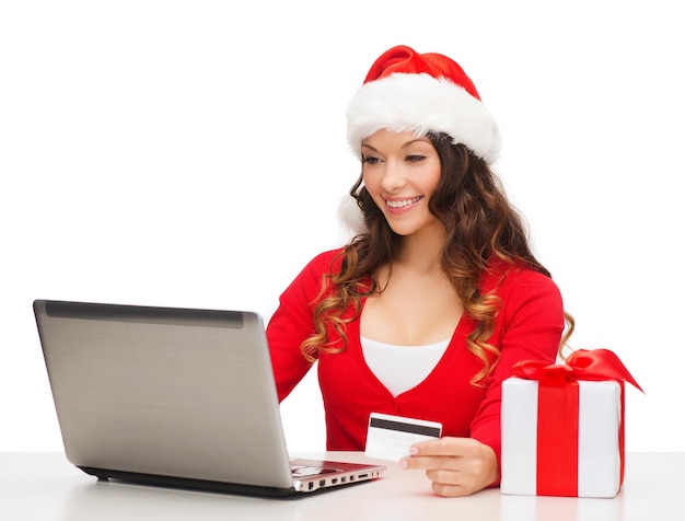 natal, natal, conceito de compras online - mulher com chapéu de ajudante de Papai Noel com caixa de presente, laptop e cartão de crédito