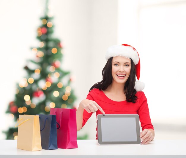 natal, natal, eletrônicos, conceito de gadget - mulher sorridente com chapéu de ajudante de Papai Noel com tela em branco do tablet pc