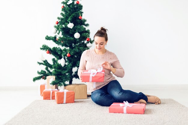 Natal, Natal, inverno, conceito de felicidade - garota abre um presente no contexto da árvore de Natal. Mulher jovem feliz comemorando o Natal