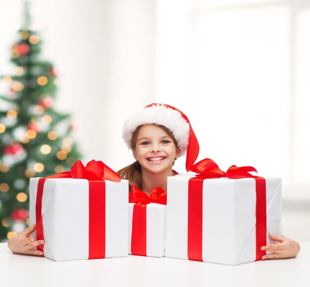 natal, natal, inverno, conceito de felicidade - menina sorridente com chapéu de ajudante de Papai Noel com muitas caixas de presente