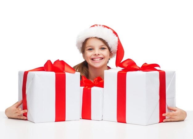 natal, natal, inverno, conceito de felicidade - menina sorridente com chapéu de ajudante de Papai Noel com muitas caixas de presente
