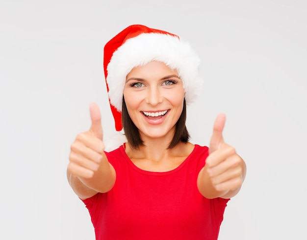natal, natal, inverno, conceito de felicidade - mulher com chapéu de ajudante de Papai Noel mostrando os polegares para cima