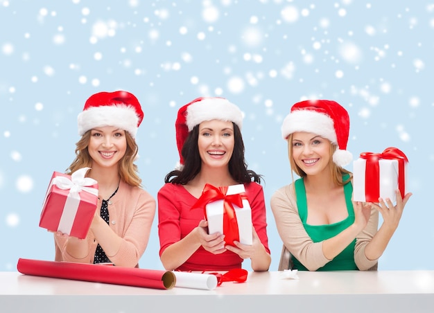 natal, natal, inverno, conceito de felicidade - três mulheres sorridentes com chapéus de ajudante de Papai Noel e caixas de presente