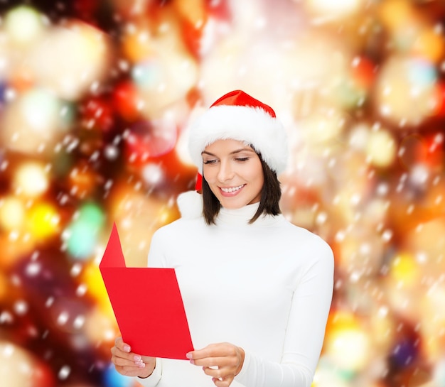 natal, natal, pessoas, propaganda, conceito de venda - mulher feliz com chapéu de ajudante de Papai Noel com cartão postal vermelho em branco