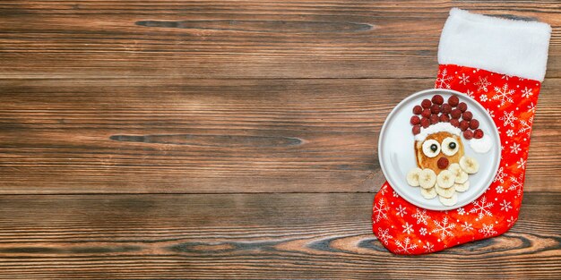 Natal papai noel em forma de panqueca com doce de framboesa fresca e banana no prato de madeira