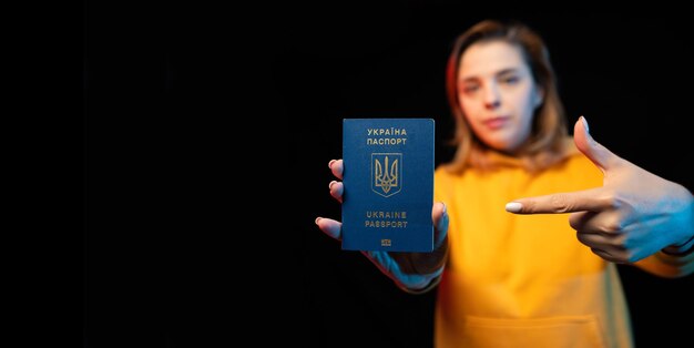 Nationaler Pass der Ukraine Schönes ukrainisches Mädchen mit Regierungspass in den Händen auf schwarzem Hintergrund