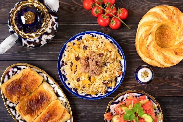 Nationaler usbekischer Pilaw mit Fleisch, Achichuk-Salat aus Tomaten, Gurken, Zwiebeln in Teller mit traditionellem