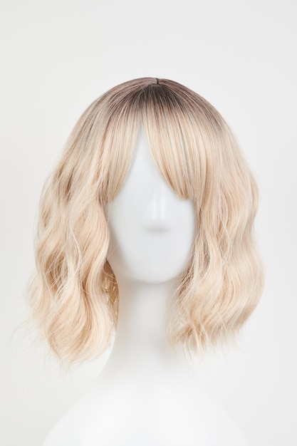 Natürlich aussehende blonde perücke auf weißem Mannequinkopf Mittellänge Haare geschnitten auf dem Plastikperückenhalter isoliert auf weißem Hintergrund Frontansicht