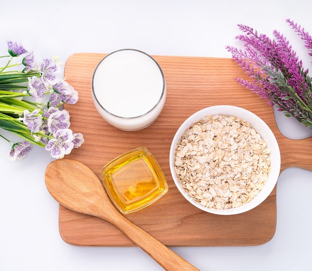 Natürliche Haferflocken, Blumen, ein Glas Milch und Honig