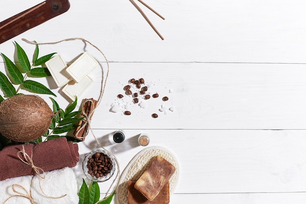 Natürliche handgemachte Seifen mit Kaffeebohnen, Zimt, Meersalz, Luffa, braunem Handtuch, Kokos und grünen Blättern auf weißem Holzhintergrund. Ansicht von oben. Platz kopieren. Stillleben. Flach liegen. SPA-Set