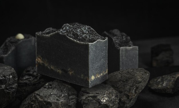 Natürliche Kohleseife auf echten Kohlen auf schwarzem Hintergrund Konzept der Herstellung und Verwendung von Bio-Öko-Seife und Kosmetik