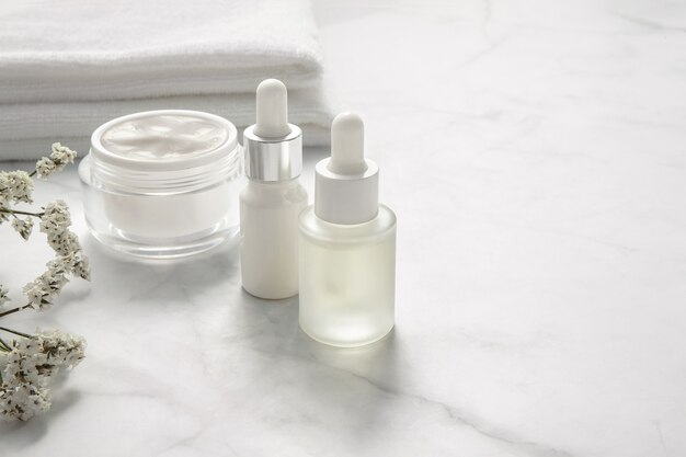Natürliche kosmetische Produkte mit Handtuch und weißen kleinen Blumen auf Marmorhintergrund.