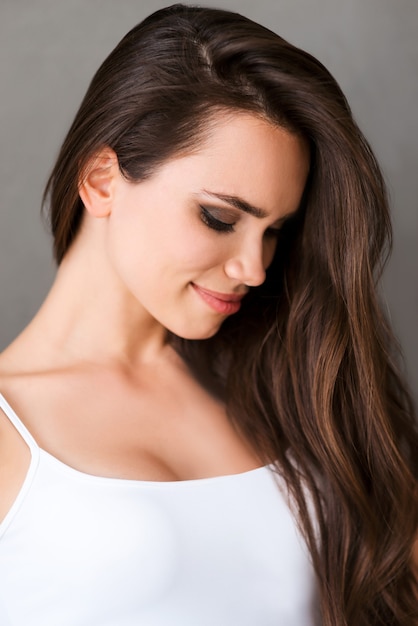 Natürliche Schönheit. Schöne junge Frau im weißen Trägershirt mit Blick nach unten