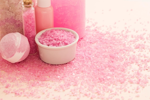 Natürliche Spa-Kosmetikprodukte Abgeschnittene Nahaufnahme von Badebombe rosa Salz in Flaschen und Kristallen, die über pfirsichfarbenem Hintergrund verstreut sind