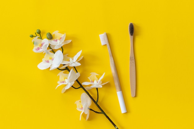 Natürliche umweltfreundliche Bambusbürsten und orhid Blume auf gelbem Papierhintergrund