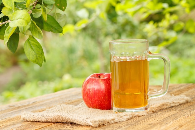 Natürlicher Apfelwein im Glasbecher und frischer roter Apfel auf Holzbrettern mit unscharfem grünem natürlichem Hintergrund. Schärfentiefe Schärfentiefe. Bio-Getränke