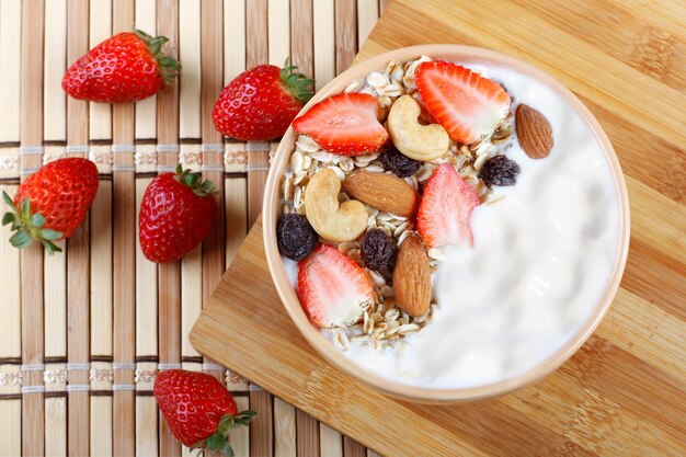 natürlicher Joghurt mit hausgemachten Granola, Erdbeeren und Nüssen in einer Keramikschüssel auf einer Tischplatte