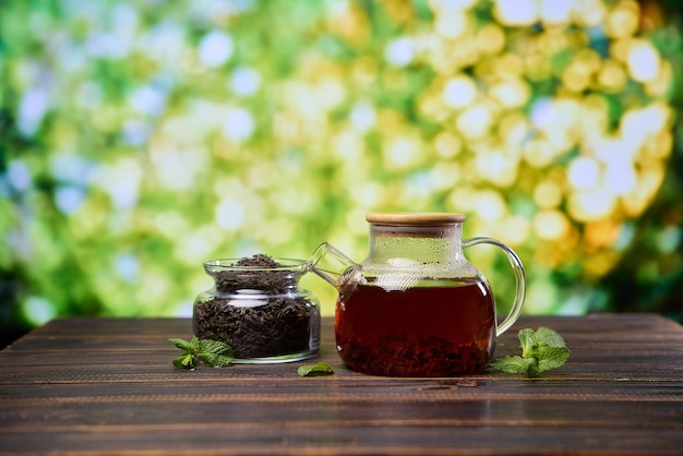 Natürlicher organischer Kräutertee in einer Glas Teekanne und einem Glas mit trockenem Tee auf einem Holztisch