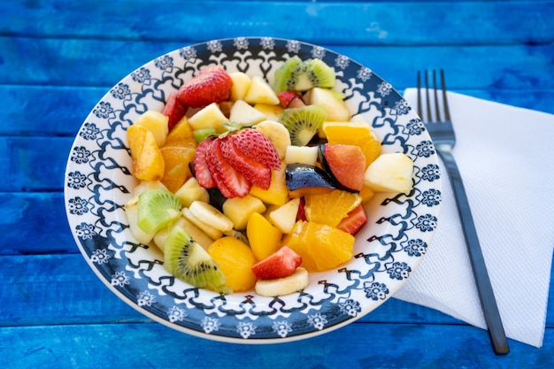 Natürlicher und gesunder Obstsalat mit Orange in einem Vintage-Teller auf einer rustikalen blauen Oberfläche.