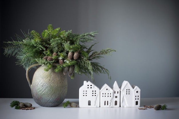 Natürlicher Weihnachtsstrauß in altem Keramikkrug mit weißen Häusern auf grauer Hintergrundwand