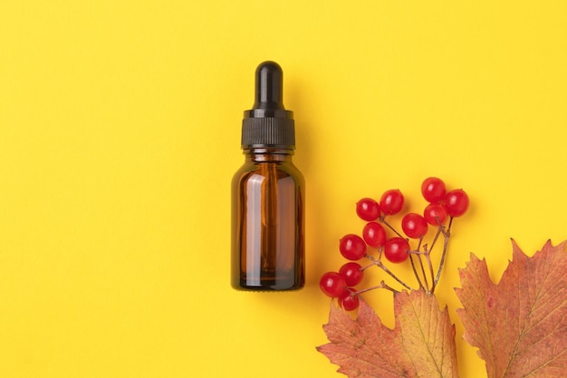 Natürliches ätherisches Öl von Viburnum in der Flasche mit einem Tropfer auf gelbem Hintergrund mit einem Zweig des herbstreifen Viburnums