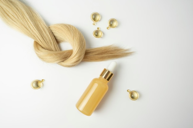 Natürliches blondes Haar und ätherisches Öl zur Haarbehandlung in goldenen Kapseln, die auf weißem Hintergrund liegen
