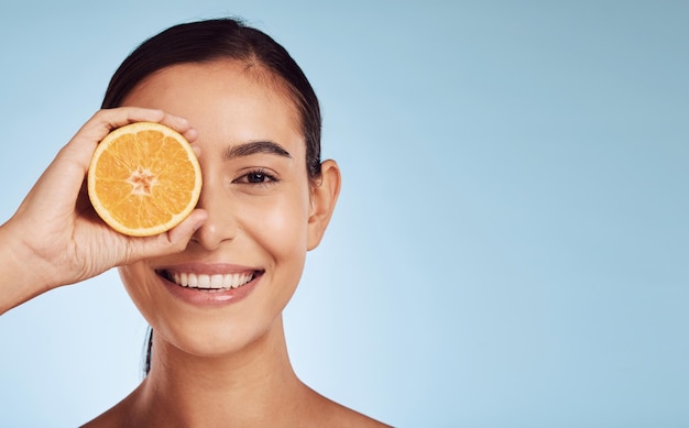 Natürliches Frauenporträt und Orange für die Hautpflege, Vitamin C oder Diät vor blauem Studiohintergrund. Person lächelt mit Bio-Zitrusfrüchten für Ernährung oder Gesichtsbehandlung auf einer Attrappe oder einem Banner