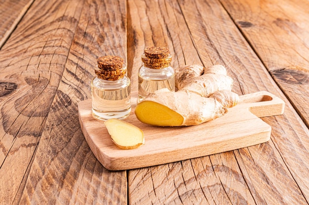 Natürliches Ingwerwurzelöl in zwei Glasflaschen mit Korkdeckel auf Holzschneidbrett und Holztisch Konzept des Heimkochens von Öl und häuslicher Körperpflege