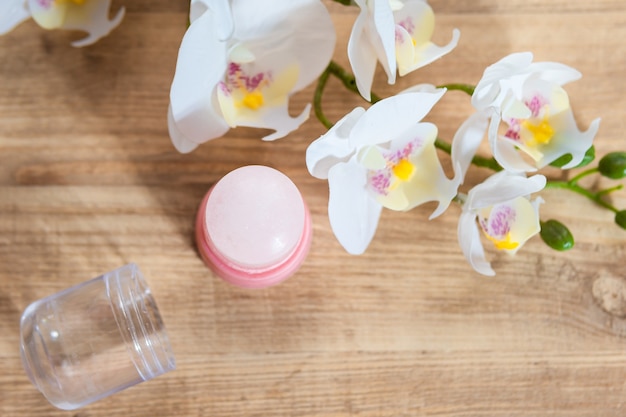 Natürliches Öko-Kristall-Alaun-Deodorant und Orchideenzweig mit Blumen auf hellem Holzhintergrund