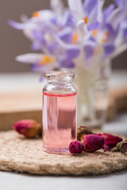 Natürliches reines Rosenöl oder duftendes Wasser in Flaschen für Spa, Hautpflege oder Aromatherapie mit trockenen rosa Rosen. Bio-Kosmetikkonzept. Selektiver Fokus