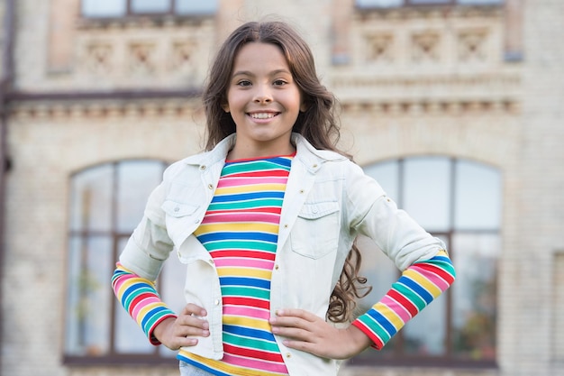 Natürliches und schönes Hipster-Kind im Freien ihr freundliches Lächeln glücklicher Kindertag kleines Mädchen hat lockiges Haar Frühlingskind Mode kleine Schönheit in positiver Stimmung Kindheit Glückskonzept