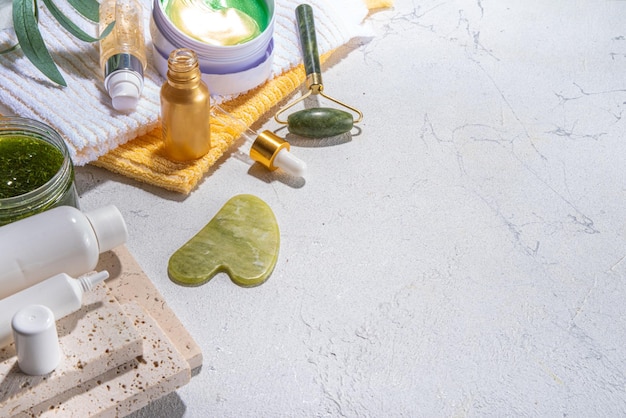 Natur-Anti-Aging-Kosmetik-Therapie-Massage Asiatische Schönheits-Hautpflege Jade-Roller Gua-Sha-Massagegerät mit verschiedenen Bio-Serum-Gel-Kräuterextrakt-Spa-Handtüchern Flatlay auf weißem Marmorhintergrund