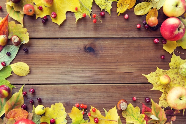 natur-, saison-, werbe- und dekorkonzept - rahmen aus herbstblättern, früchten und beeren auf holztisch