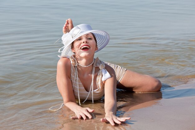 Natur, Schönheit, Jugend und gesundes Lebensstilkonzept. Frau in einem gestreiften Retro-Badeanzug mit weißem Regenschirm und weißem Hut gegen das Meer