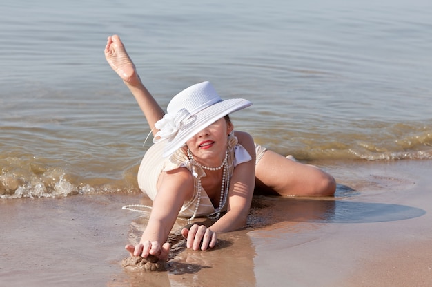 Natur, Schönheit, Jugend und gesundes Lebensstilkonzept. Frau in einem gestreiften Retro-Badeanzug mit weißem Regenschirm und weißem Hut gegen das Meer