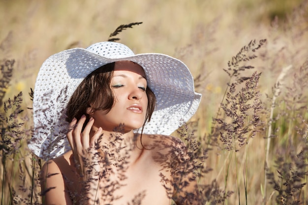 Natur, Schönheit, Jugend und gesundes Lebensstilkonzept. Junge Frau im weißen Hut auf Naturrasenhintergrund. Mädchen, das draußen die Natur genießt.