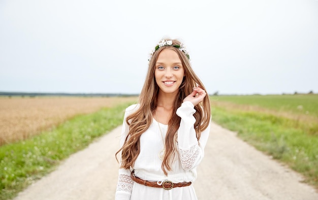 Natur-, Sommer-, Jugendkultur- und Menschenkonzept - lächelnde junge Hippie-Frau mit Blumenkranz auf Getreidefeld