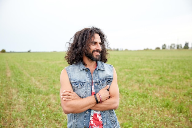 Natur-, Sommer-, Jugendkultur- und Menschenkonzept - lächelnder junger Hippie-Mann in Jeansweste auf der grünen Wiese