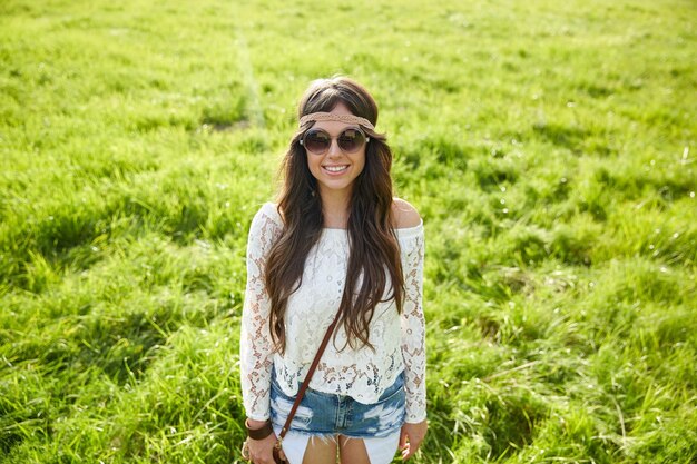 Natur, Sommer, Jugendkultur und People-Konzept - lächelnde junge Hippie-Frau mit Sonnenbrille auf der grünen Wiese